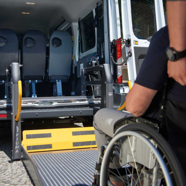 Person im Rollstuhl fährt auf herausgeklappten Rollstuhllift auf